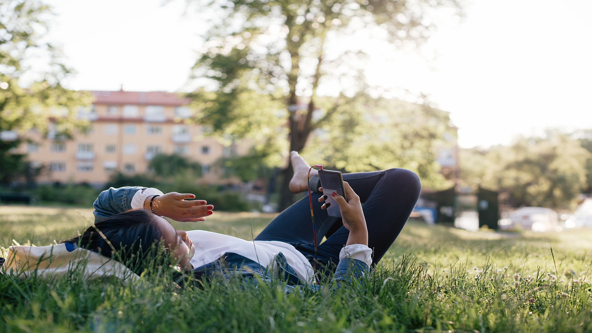 Fotograf: Johnér. Ligger i gräset och tittar på mobiltelefonen.